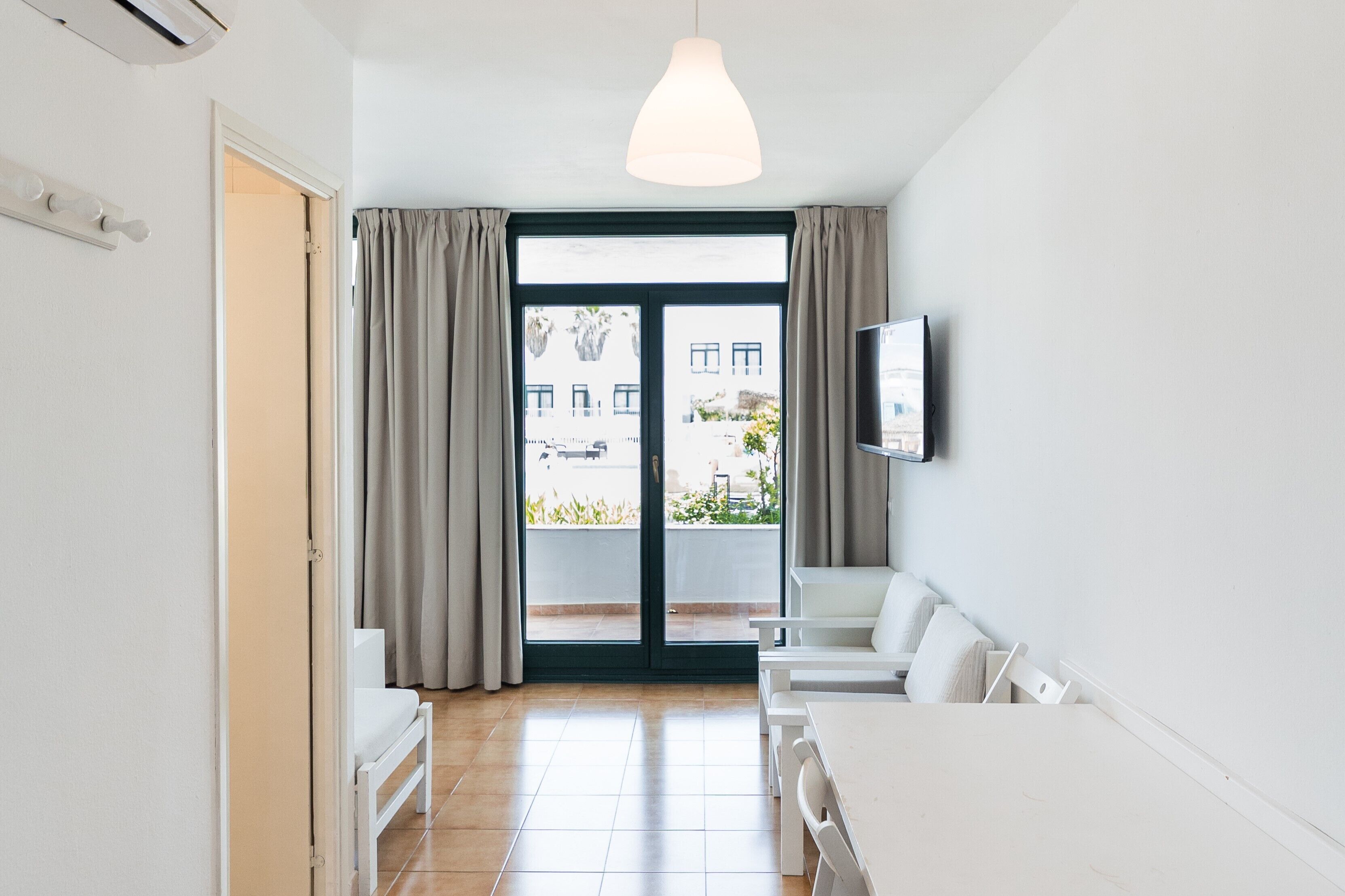 Een moderne kamer met een schuifdeur naar een balkon, witte meubels en een wandtelevisie.
