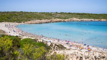 Une plage à l’eau d’un bleu limpide, aux rivages sablonneux et parsemée de nombreux parasols colorés.