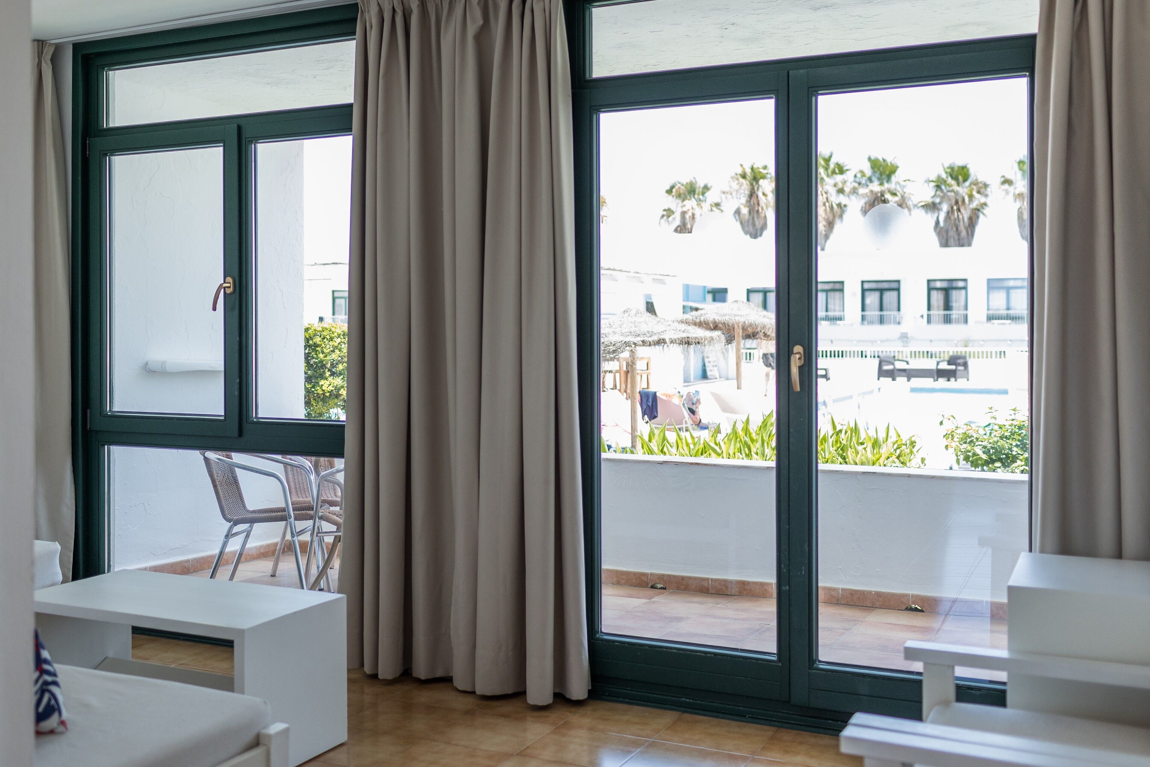 Ein Zimmer mit einer großen Schiebeglastür, die auf einen Balkon mit Gartenmöbeln und Pflanzen führt.