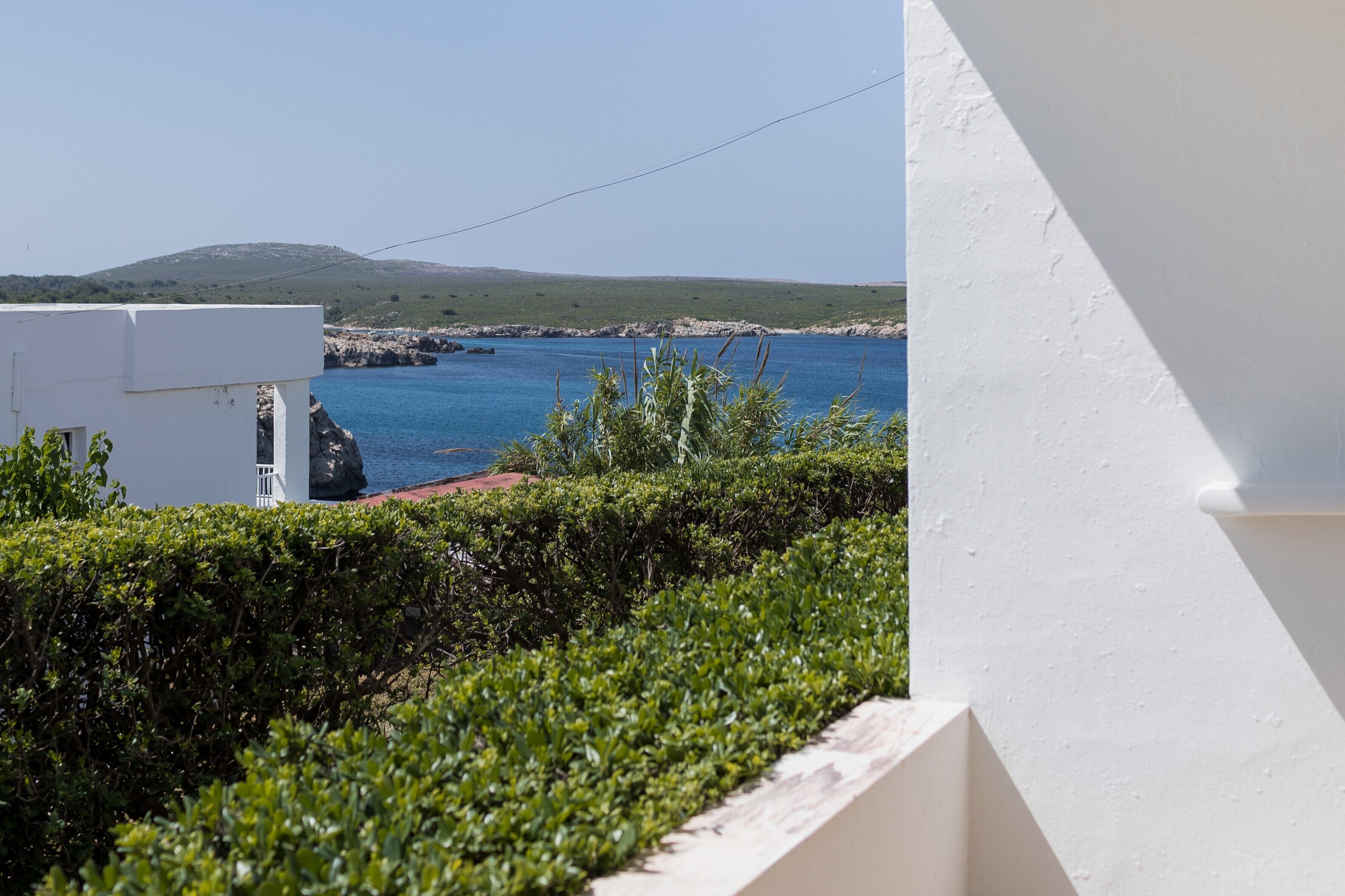 Vista costera con un edificio blanco, una costa rocosa y un mar azul claro.
