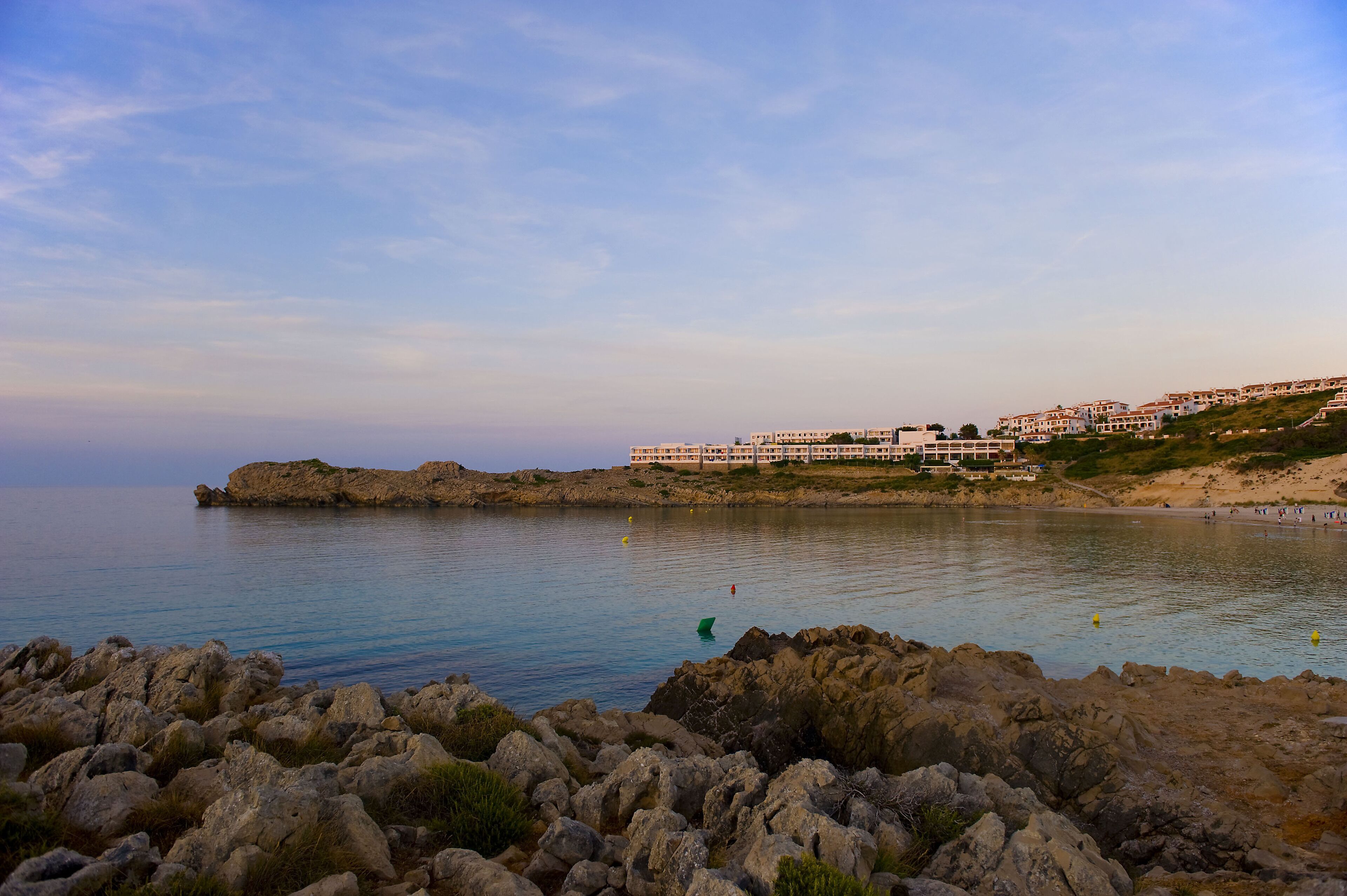A coastal hotel with multiple buildings, rocky shoreline, and calm sea.