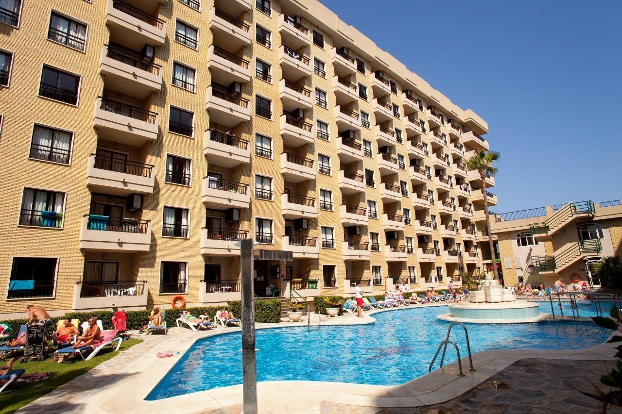A multi-story hotel with a swimming pool and sun loungers.