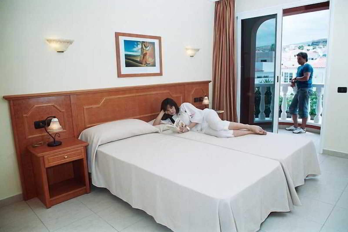 A hotel room with two beds, a nightstand, a lamp, and a painting on the wall.