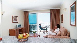 A hotel room with a dining area, a television, a fruit bowl, and a balcony with a view. - Callaomar (Adeje)