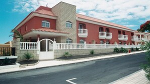 A large, multi-story building with a red facade, multiple balconies, and a gated entrance. - Callaomar (Adeje)
