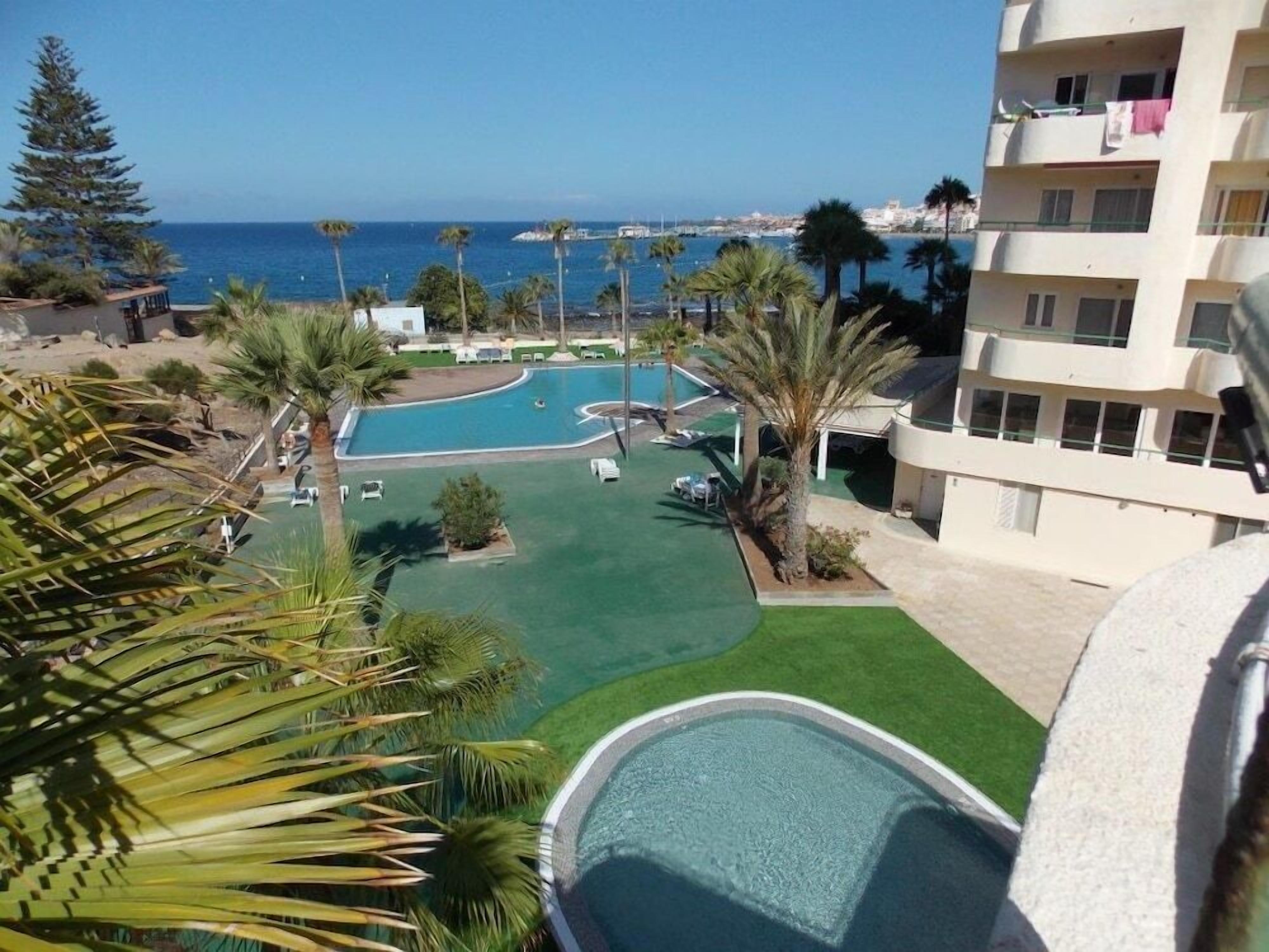 A resort with a pool area, palm trees, and a view of the sea.