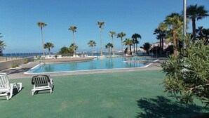 A pool area with lounge chairs and palm trees. - Apartamentos Costamar (Arona)