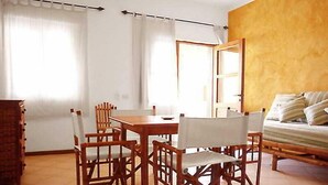 Ein Essbereich mit Holztisch und Stühlen, einer Couch und einem Fenster mit Vorhängen.