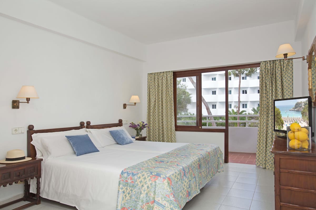 Une chambre d’hôtel comprenant un lit, une table de chevet, une commode, une télévision et un balcon avec vue sur la mer.
