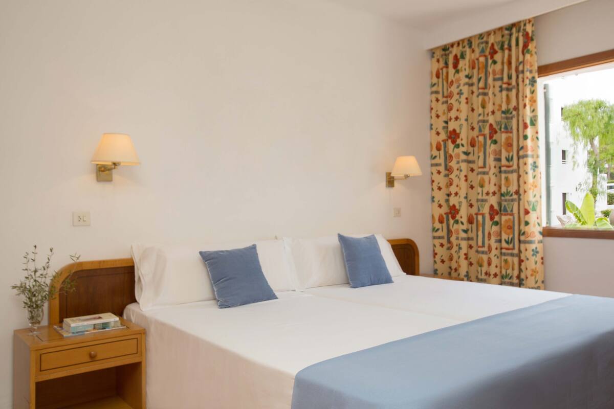 Une chambre à coucher avec un lit, des tables de chevet, des lampes et une fenêtre avec des rideaux.