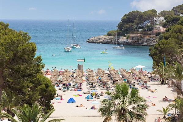 A beach with numerous umbrellas and sun loungers, a rocky coastline, and boats in the water. - Gavimar Cala Gran Costa Del Sur (Santanyi)