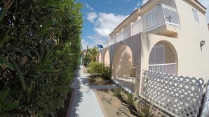 A building with a balcony, arched windows, and a pathway lined with plants. - Bungalows Parque Nogal (San Bartolomé de Tirajana)