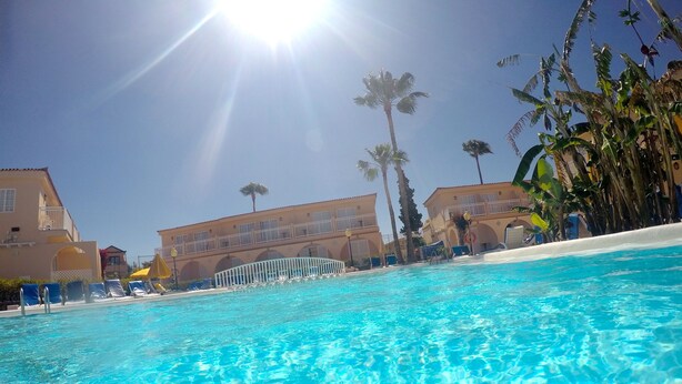A clear blue pool with lounge chairs and palm trees in the background. - Bungalows Parque Nogal (San Bartolomé de Tirajana)