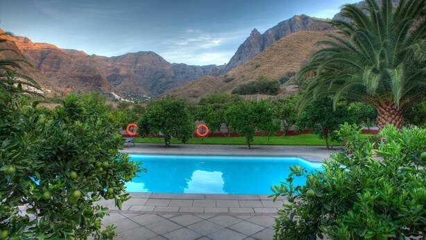 Ein Pool mit Bergblick, umgeben von Grünflächen und Palmen.