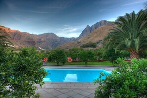 A swimming pool with a view of mountains, surrounded by greenery and palm trees. - Hotel Rural Las Longueras (Agaete)