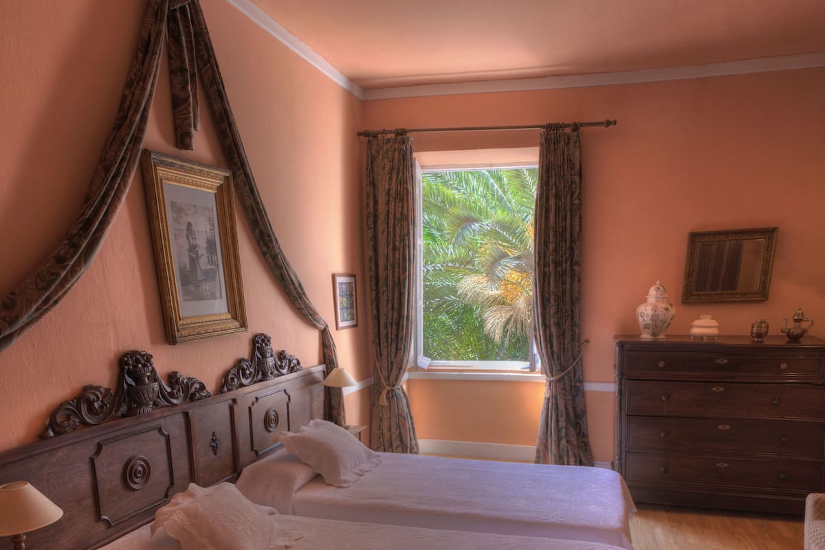 A bedroom with two beds, a dresser, a nightstand, and a window with curtains.