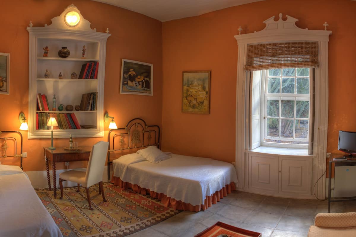 A bedroom with two single beds, a desk with a chair, a bookshelf, and a television on a stand.