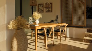 A dining area with a wooden table, chairs, hanging wicker lamps, and a vase with dried flowers. - Paya Suites (Formentera)