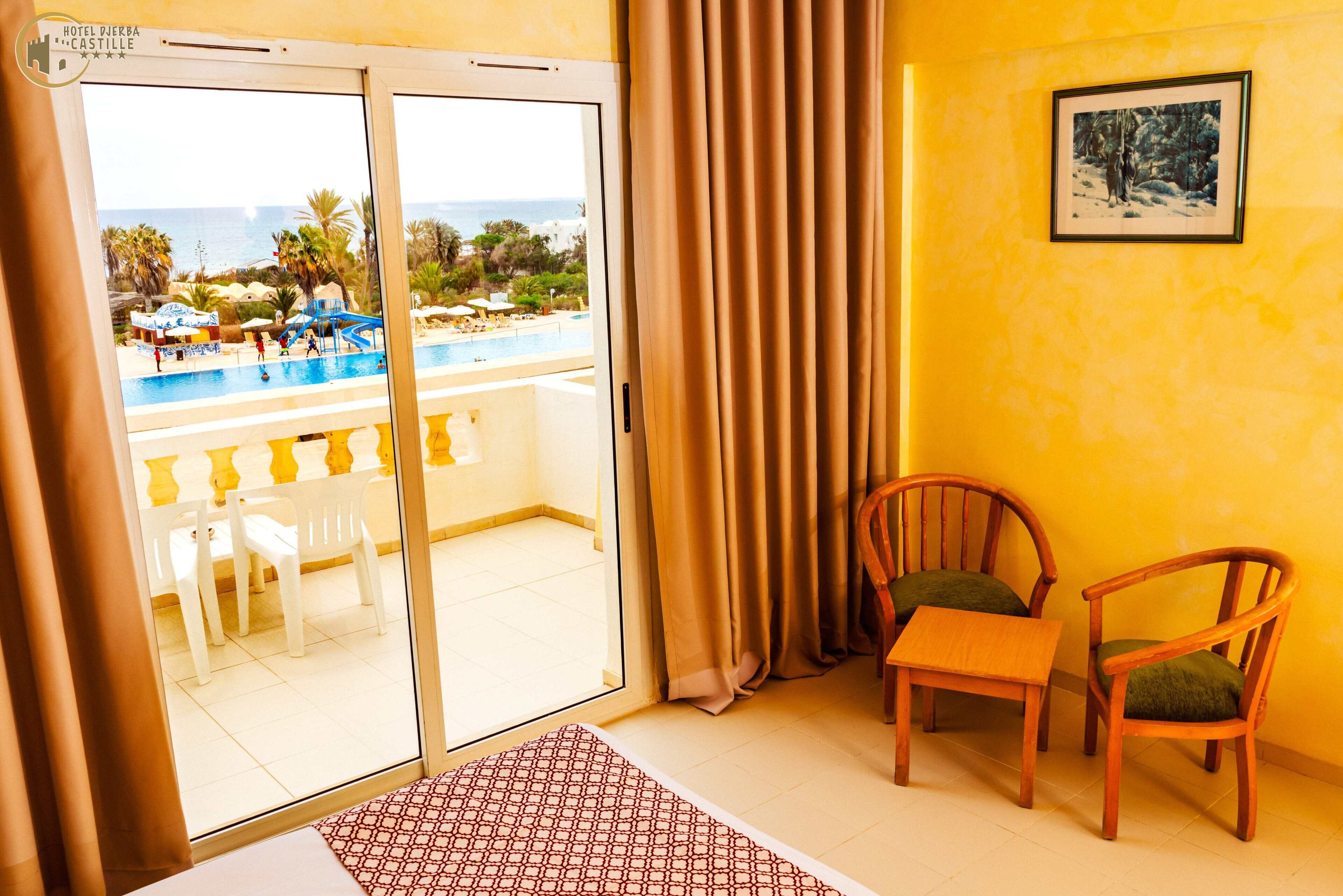 A hotel room with a sliding glass door leading to a pool area, two wooden chairs, and a framed picture on the wall.