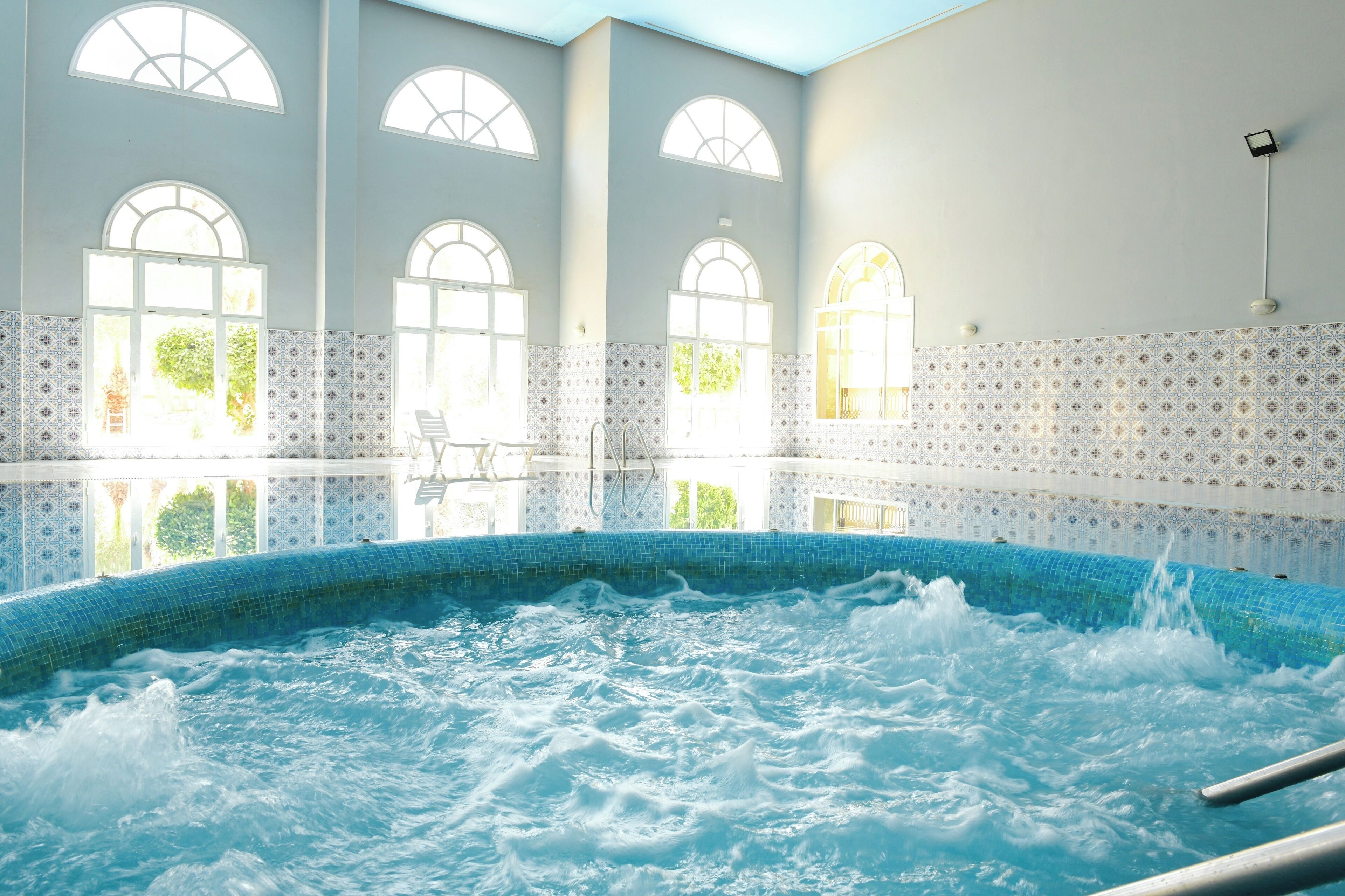 Un espacio de spa con jacuzzi, ventanas de arco y paredes de azulejos con diseños.