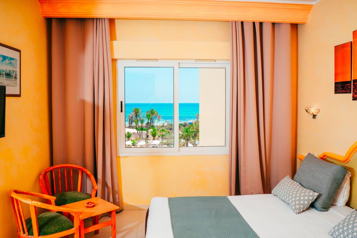 Una habitación de hotel con cama, una silla, una mesa y ventana con vista a la playa y al océano.