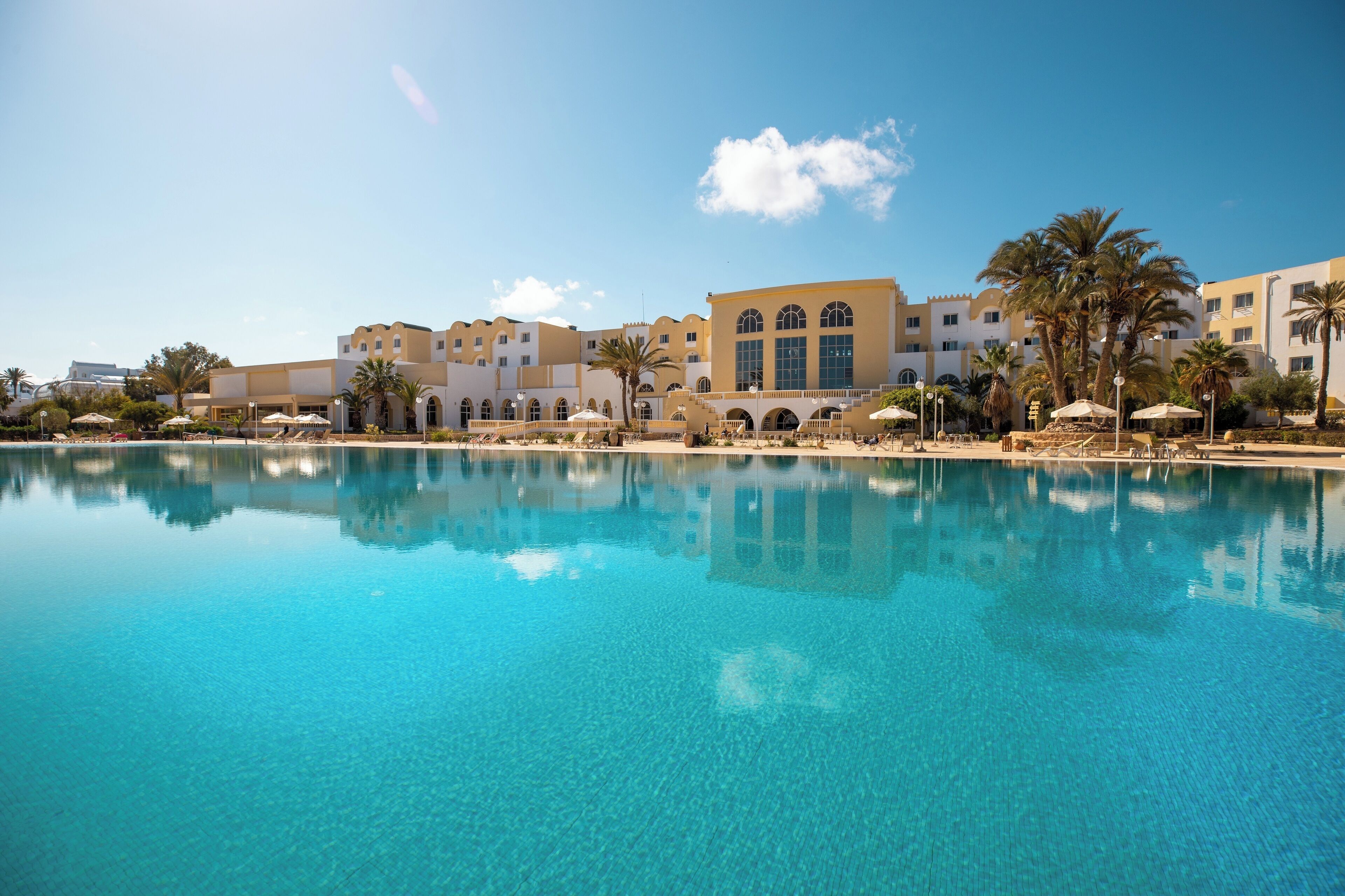 A resort with a large pool, palm trees, and Mediterranean-style buildings.