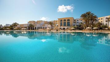 A resort with a large pool, palm trees, and Mediterranean-style buildings.