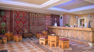 Un hall d’entrée avec des tapis à motifs, des meubles en bois et un comptoir de réception agrémenté de narguilés.
