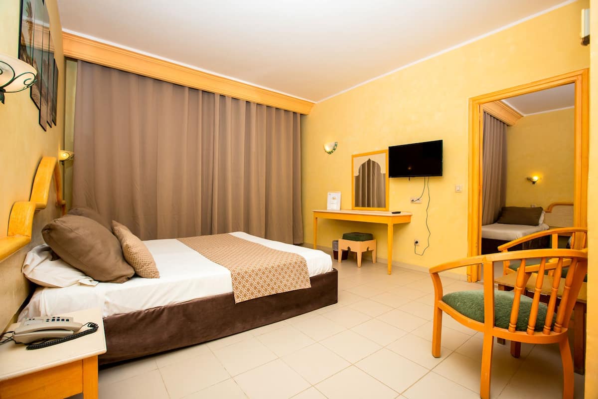 Una habitación de hotel con cama, escritorio, silla, televisión y espejo.