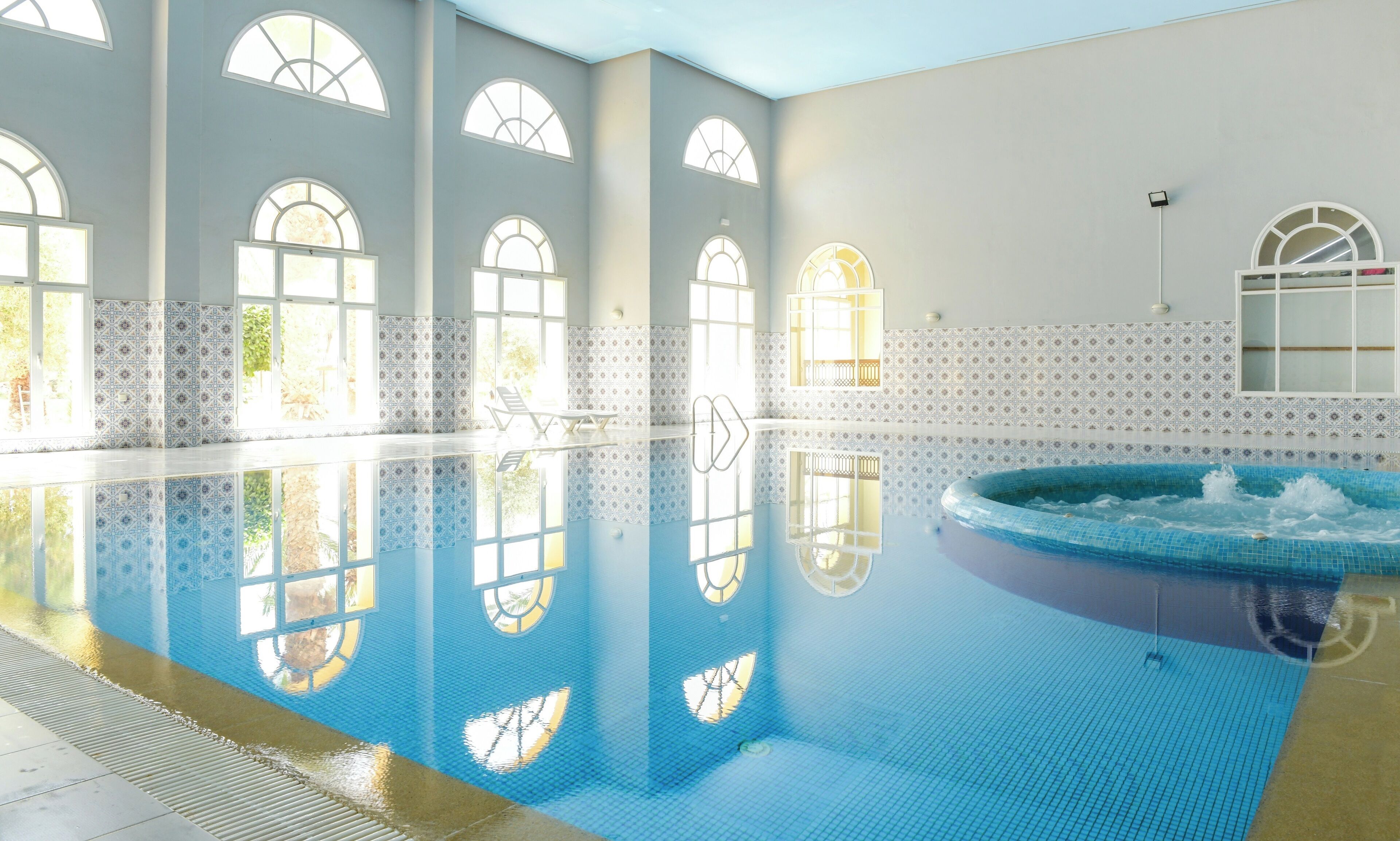 Una amplia piscina interior con reflejos cristalinos, ventanas en arco y paredes de azulejos.