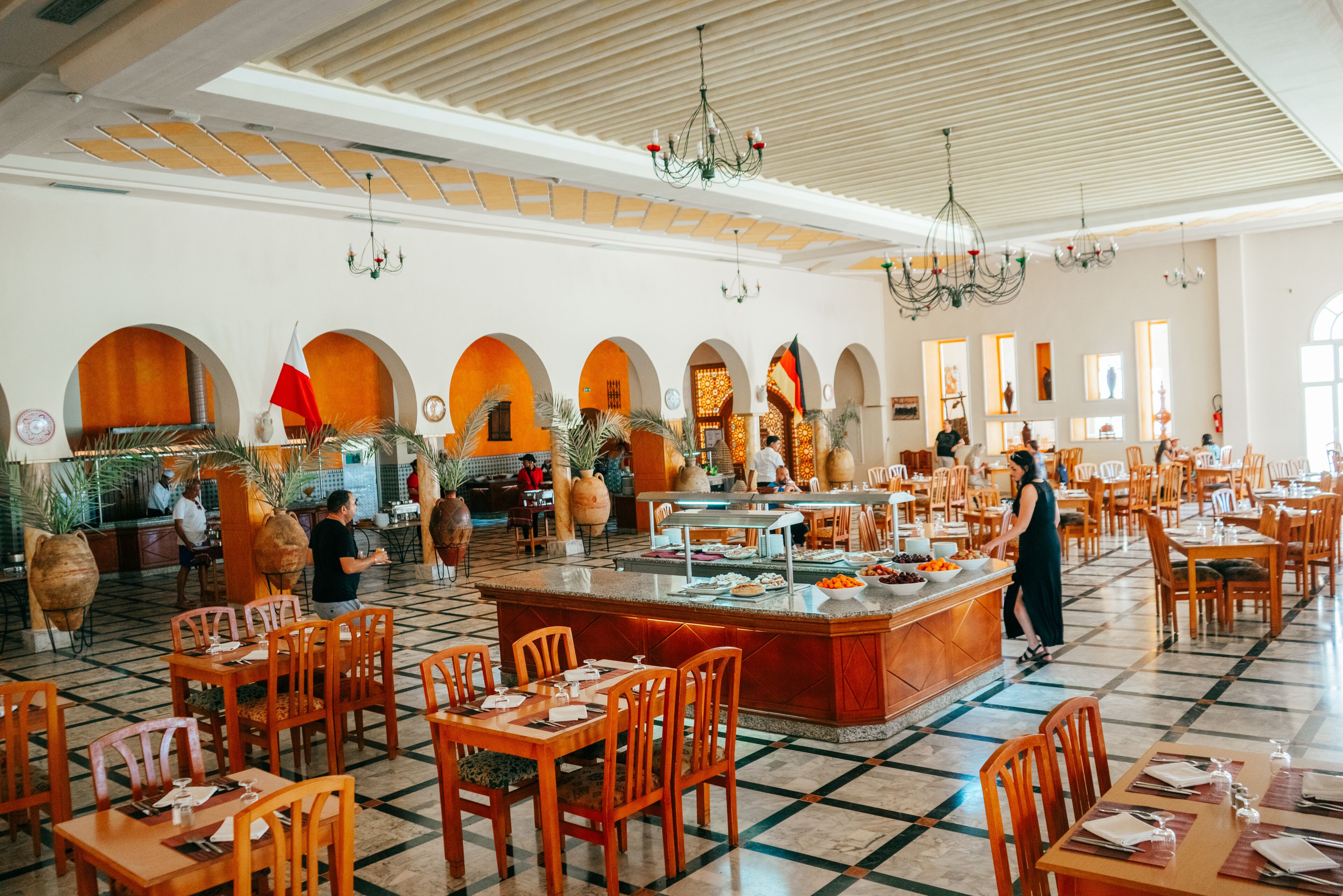 A spacious dining area with multiple tables and chairs, a central buffet, and decorative vases.