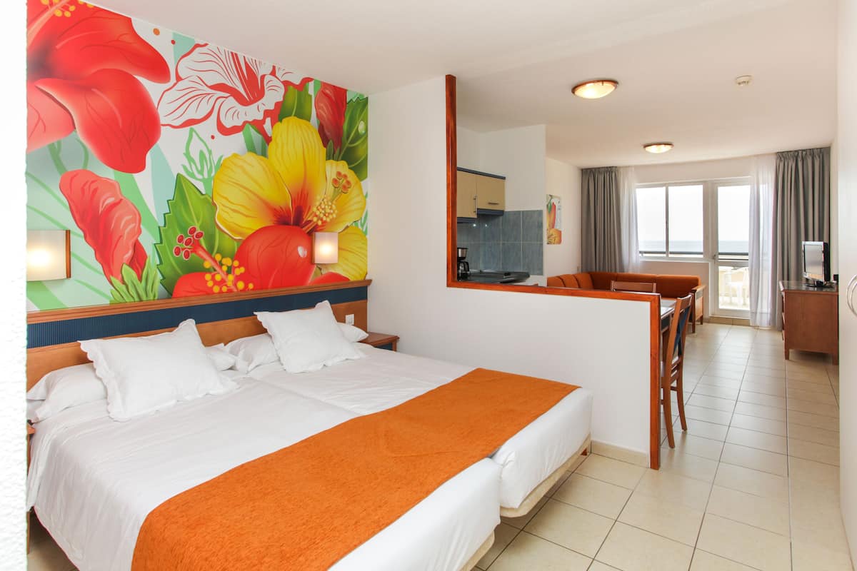 A hotel room with a large bed, a dining area, and a kitchen in the background.