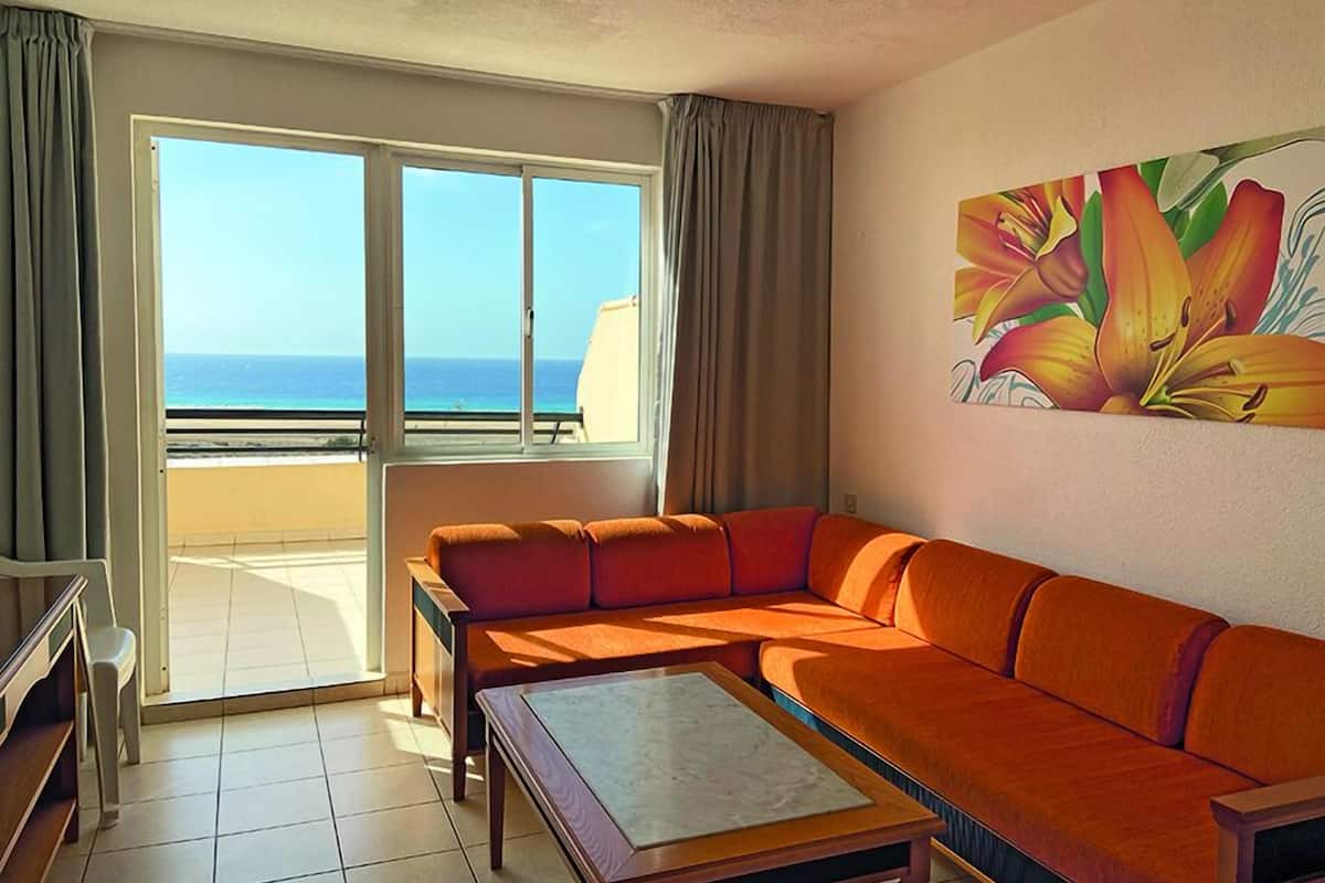A room with a large window, a sofa, a coffee table, and a painting of flowers.