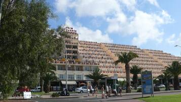 Un hotel grande con varios pisos y balcones, rodeado de palmeras y un cielo despejado.