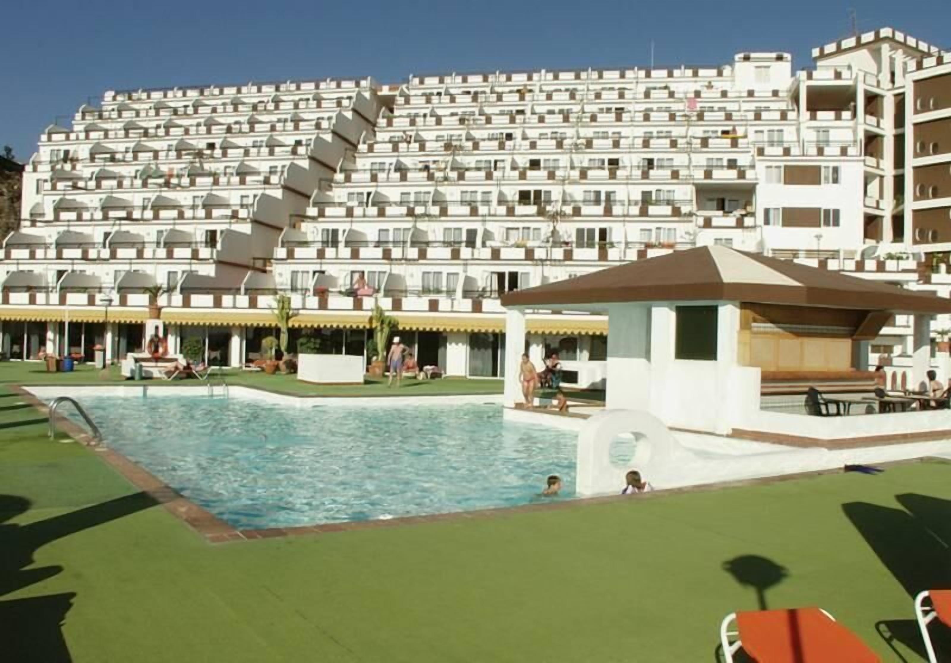 A hotel with a swimming pool, multiple balconies, and a covered seating area.