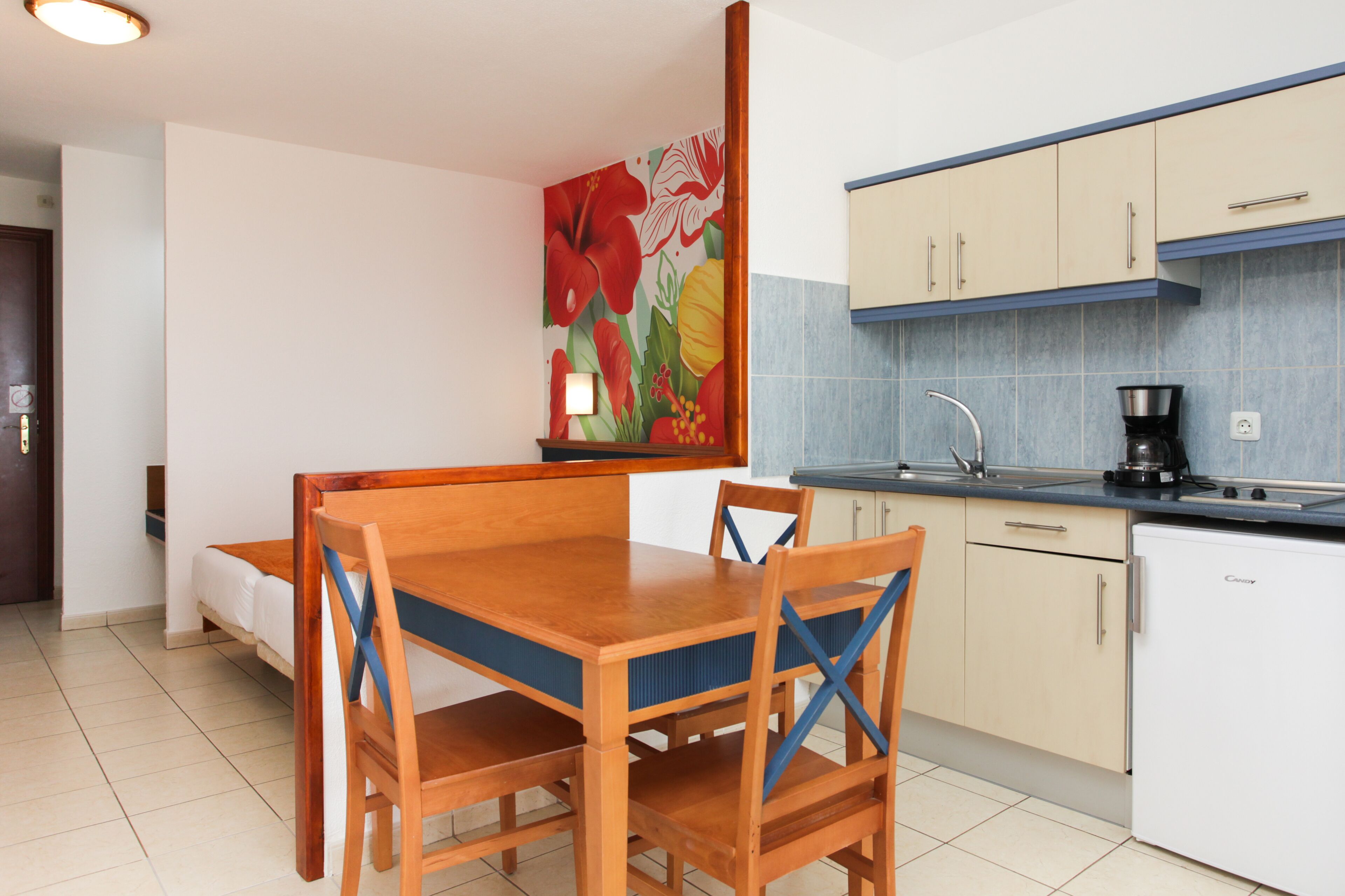 Une cuisine compacte comprenant un coin repas, un lit et un mur orné d’une fresque florale.