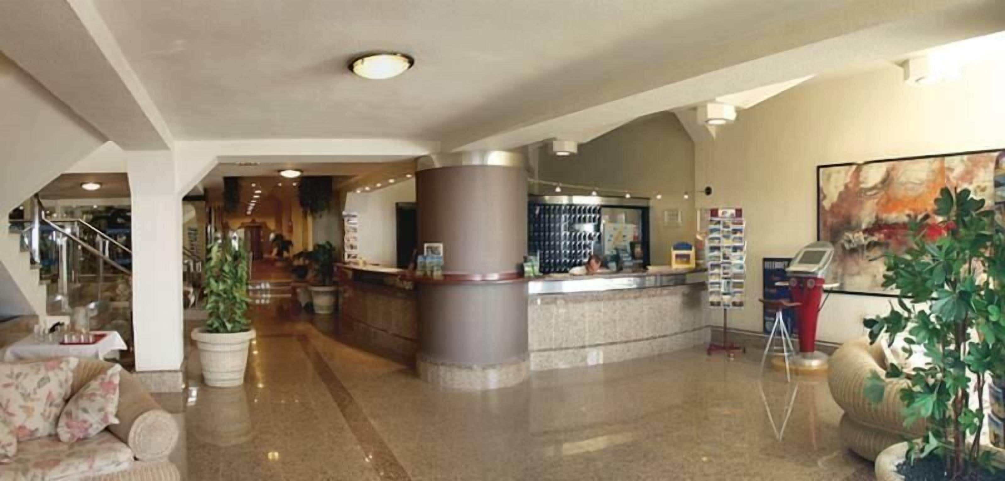 A hotel lobby with a reception desk, a staircase, and a seating area with a sofa.