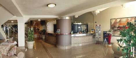 A hotel lobby with a reception desk, a staircase, and a seating area with a sofa.