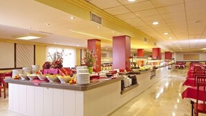 Un buffet composé de plusieurs points de service, d’un long comptoir et d’une rangée de tables recouvertes de nappes rouges.