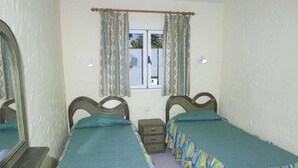 A bedroom with two single beds, a small bedside table, a mirror, and a window with curtains. - Bungalows Las Tartanas III (San Bartolome de Tirajana)