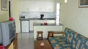 A compact living space with a kitchenette, a sofa, a coffee table, and a television. - Bungalows Las Tartanas III (San Bartolome de Tirajana)