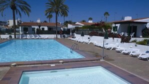 A rectangular swimming pool with a ladder, surrounded by white lounge chairs and palm trees. - Bungalows Las Tartanas III (San Bartolome de Tirajana)