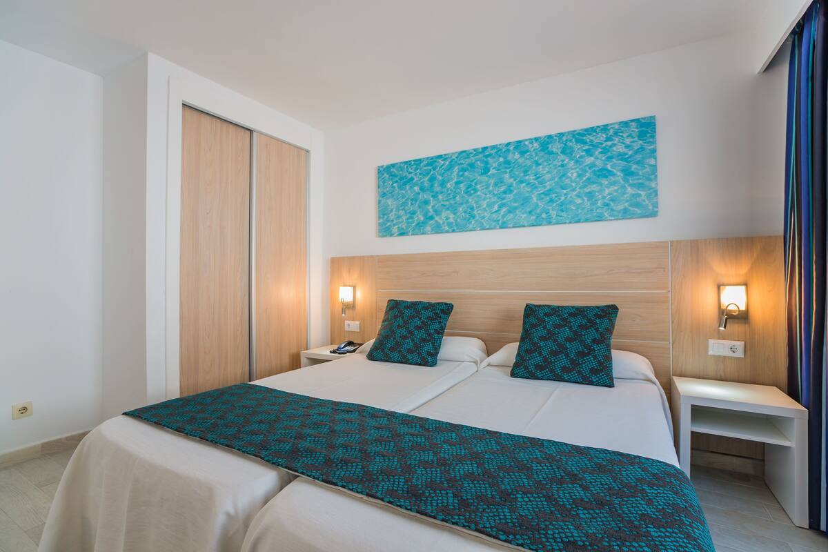 A hotel room with a large bed, two bedside tables, a nightstand, a wooden headboard, and a wall-mounted artwork.