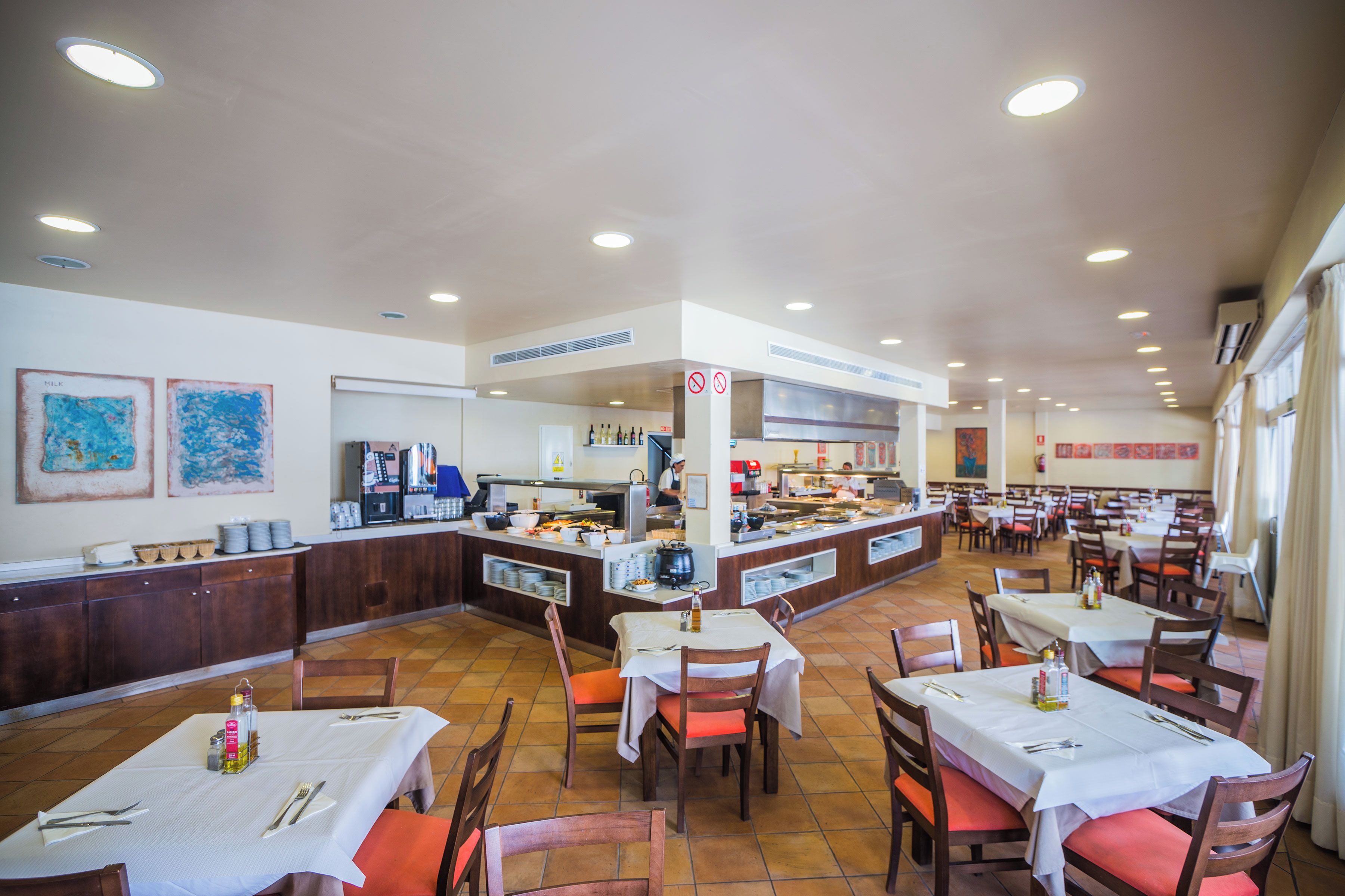 Un restaurant doté de plusieurs tables, d’un comptoir central avec une machine à café et d’œuvres d’art accrochées aux murs.