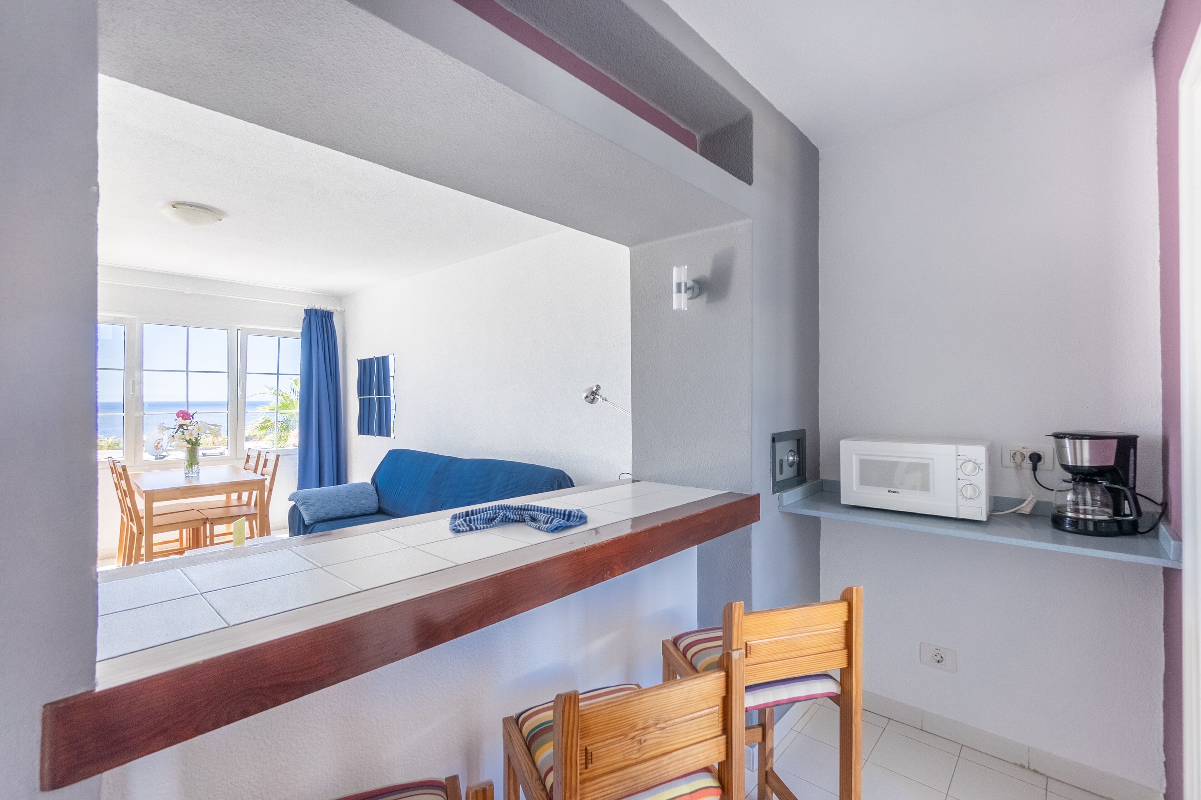 A kitchen with a wooden countertop, a microwave, a coffee maker, and a dining area with chairs and a table.