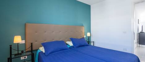 Een tweepersoonsbed met een geborduurde hoofdbank, twee nachtkastjes met lampen, en een wand in turquoise.