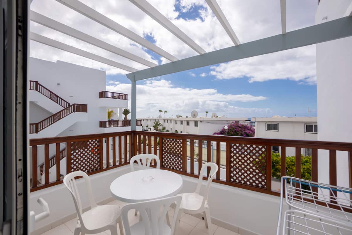 A balcony with a white table and chairs, wooden railings, and a view of buildings and sky.