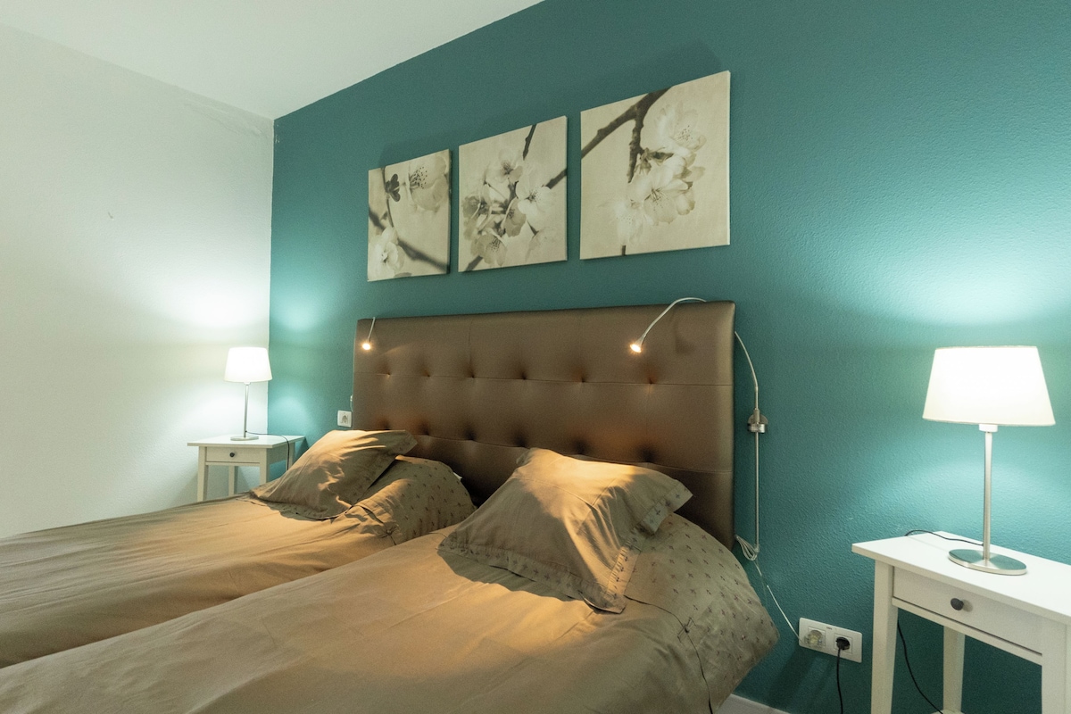 A bedroom with a double bed, two bedside tables with lamps, and three wall-mounted artworks.
