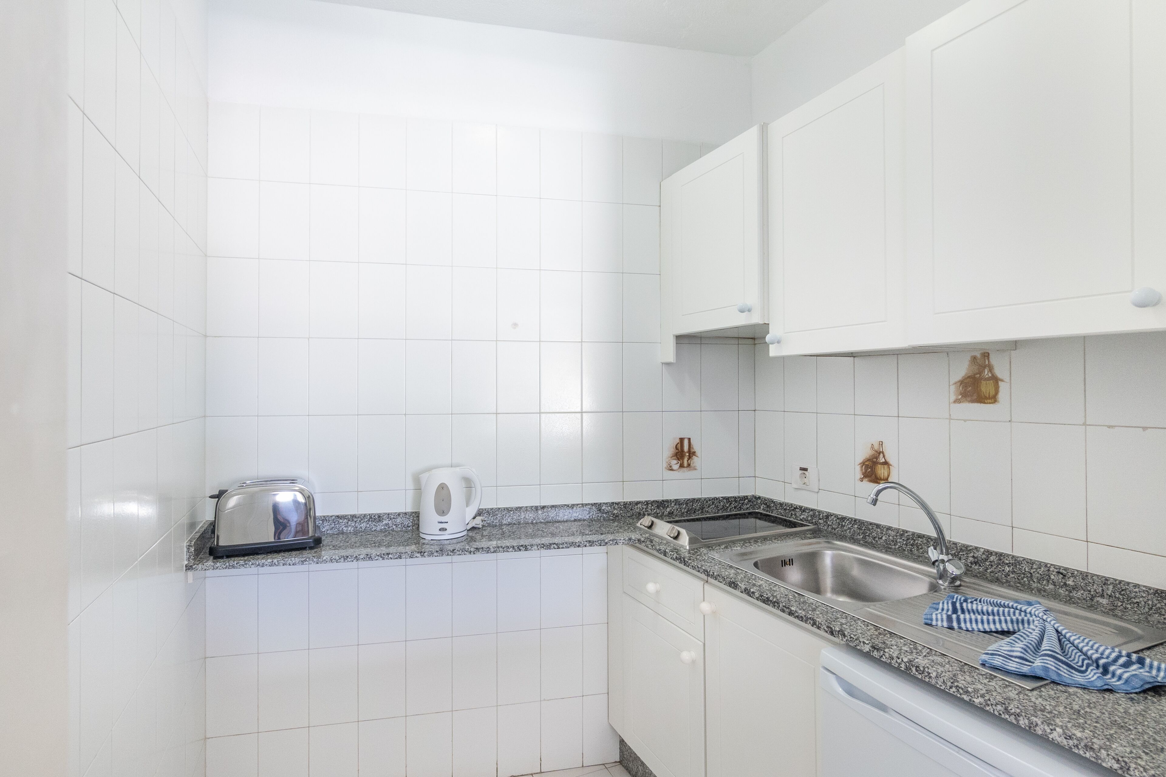 A kitchen with white cabinets, a granite countertop, a toaster, a kettle, and a sink.