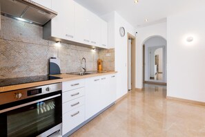 A modern kitchen with white cabinets, a stainless steel oven, a sink, and a clock on the wall. - Las Floritas (Arona)